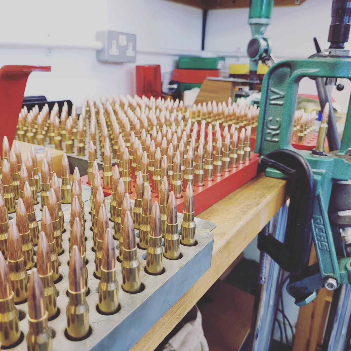 Trays of freshly assembled rounds on a workshop bench beside a green reloading press