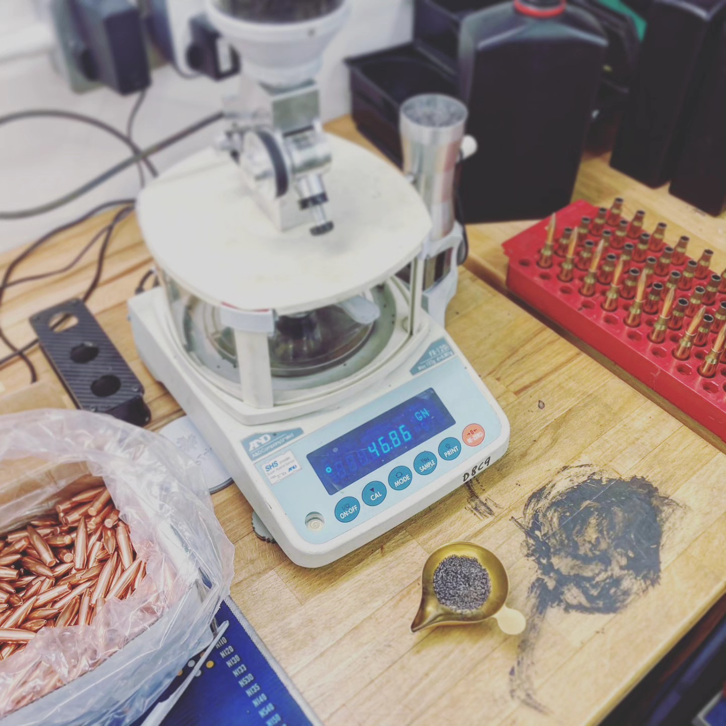 A digital powder scale reading 46.86 grains, with a bag of bullets and a tray of primed cases alongside
