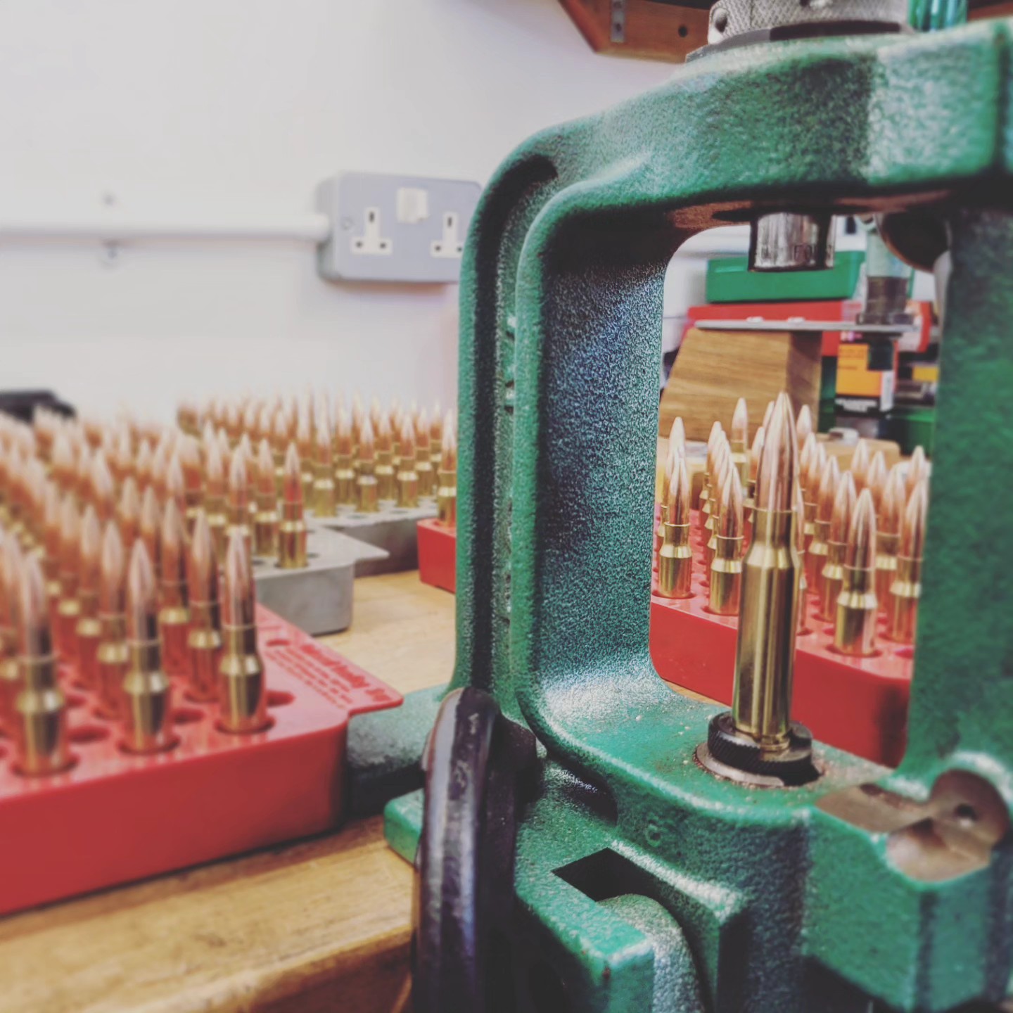 A cartridge held in the die of a green reloading press, loading blocks of finished rounds behind it