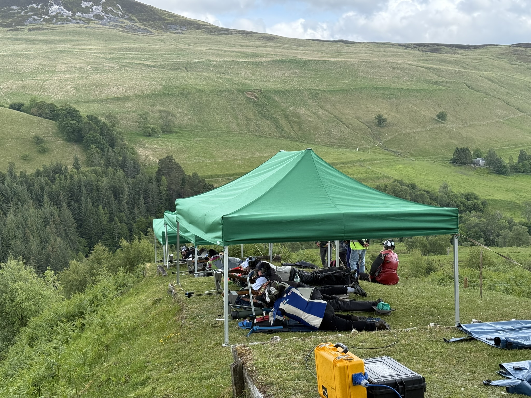 Competitors shooting from beneath green gazebos on the hillside firing point at Blair Atholl