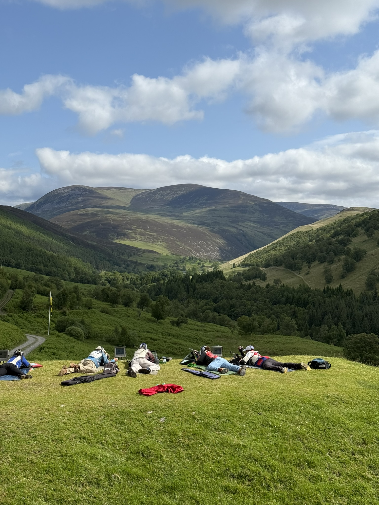 Shooters spread along the firing point at Blair Atholl beneath a wide blue sky and rolling hills