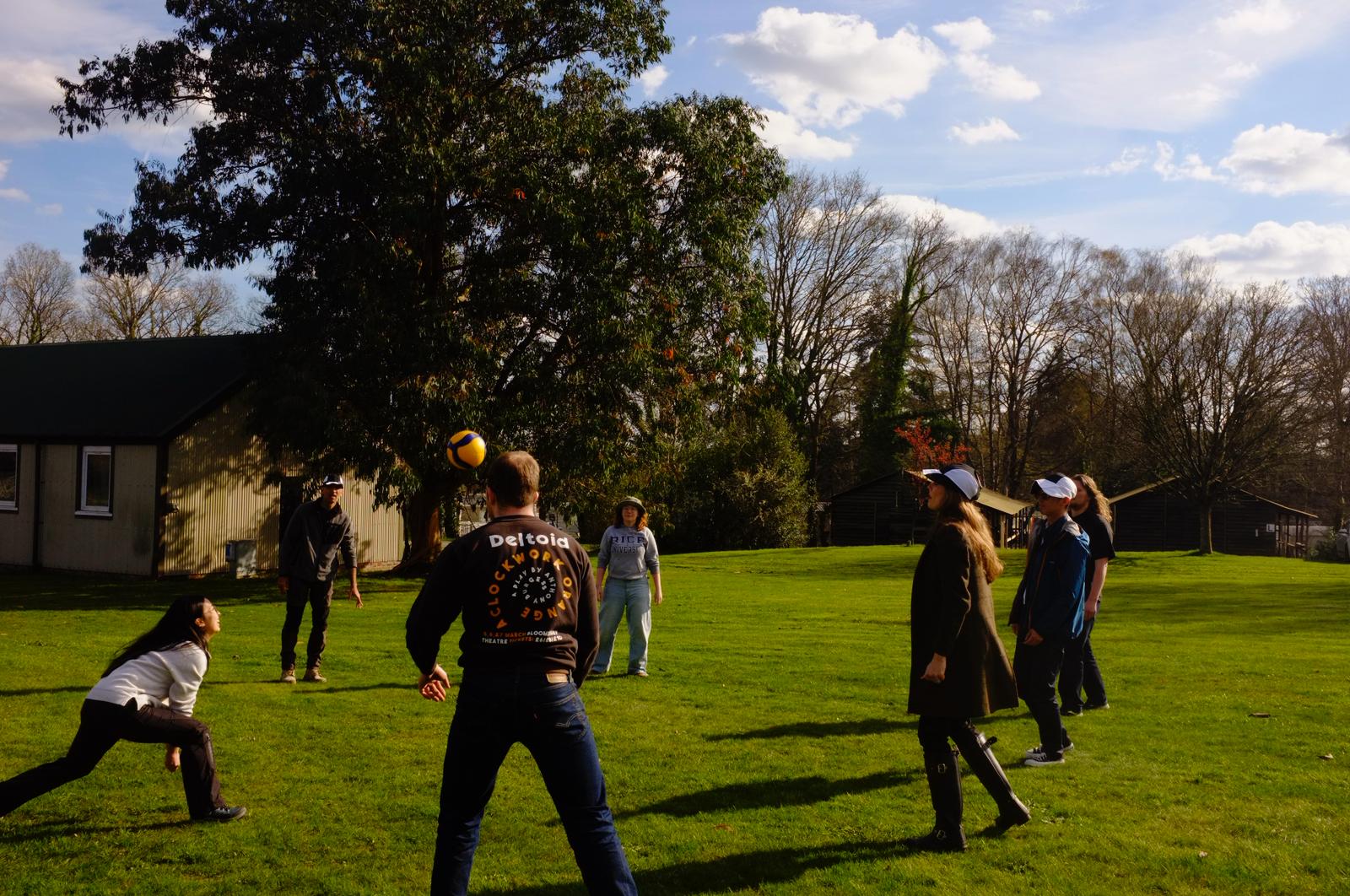 Members playing volleyball on the grass outside the huts at Bisley in the late afternoon sun